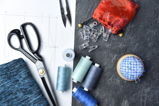 Matériel de couture pour une trousse d'écolier : ciseaux, fils, épingles et tissu sur une surface de travail.