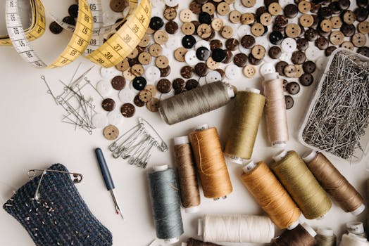 Matériaux de couture avec bobines de fil colorées, boutons et épingles sur une table de travail.