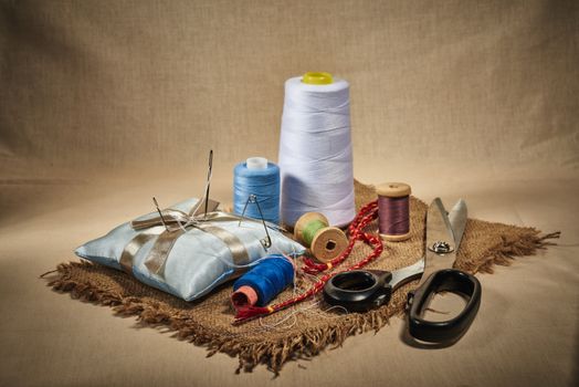 Matériel de couture avec fils colorés, ciseaux, épingles et un coussin à épingles sur un tissu en toile.